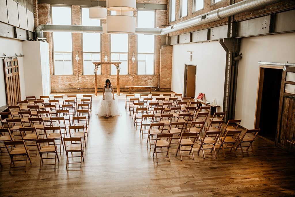 bride walking in empty loft venue ceremony space for her first look with her groom