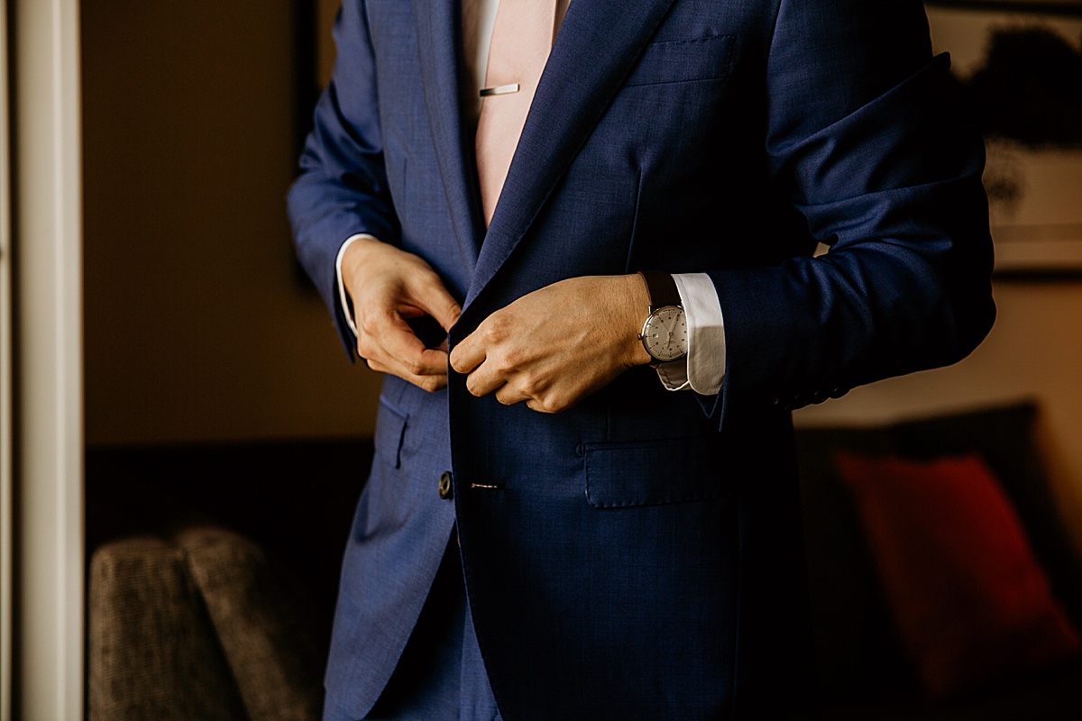 groom buttoning his navy blue suit jacket