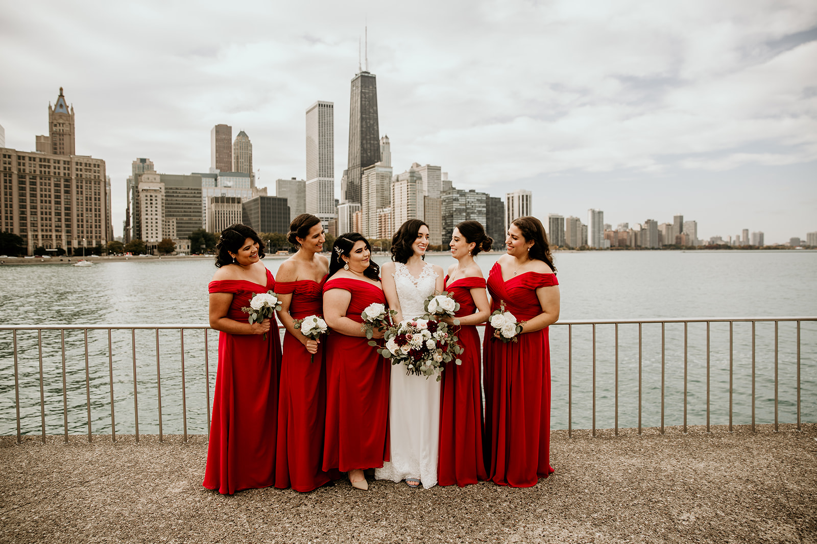 Bride and bridesmaids in red dresses looking at each other in front of the chicago skyline.