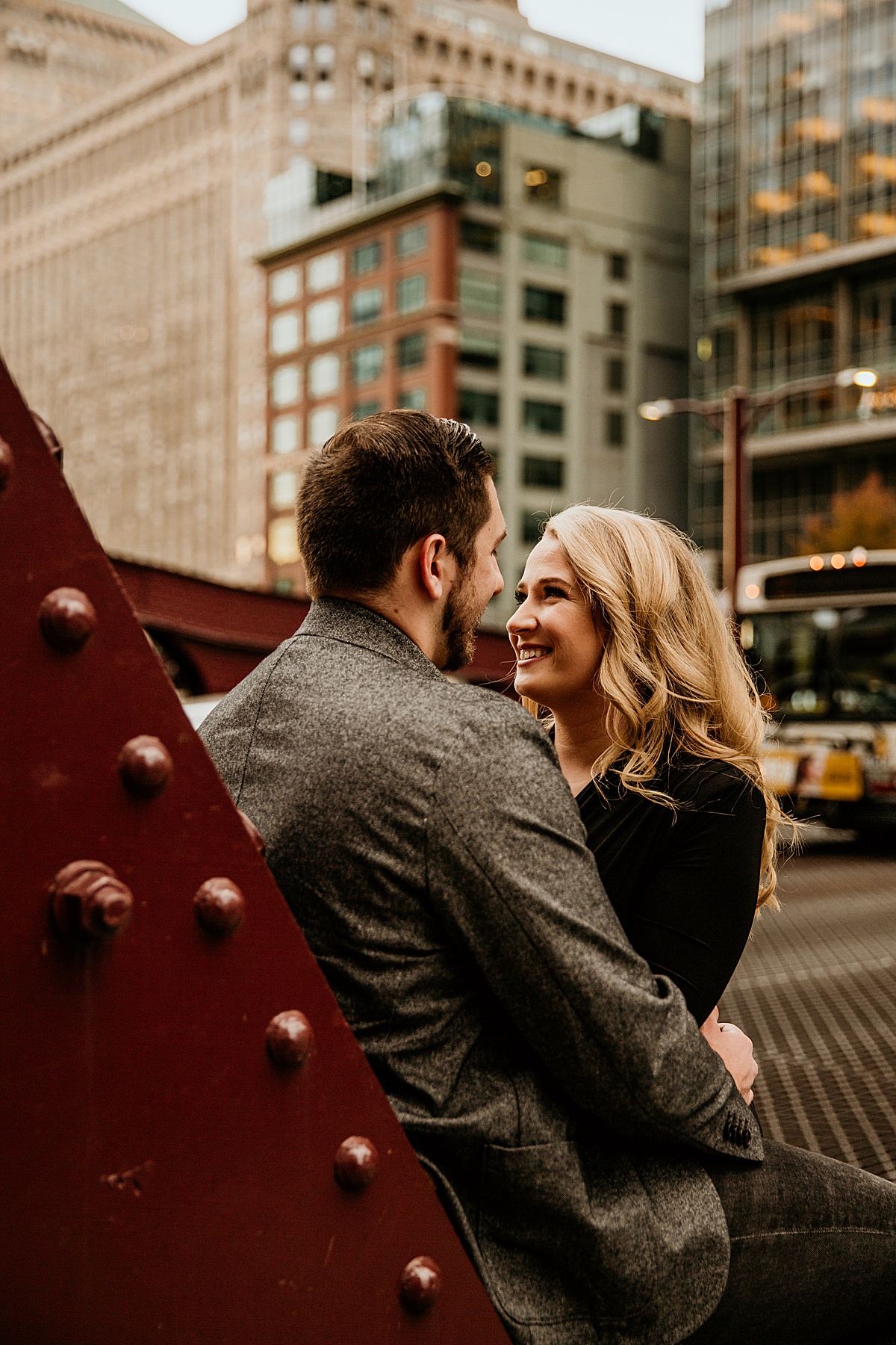 Man leaning on a bridge in Chicago and his fiancé is leaning on him, holding his face while they look at each other.