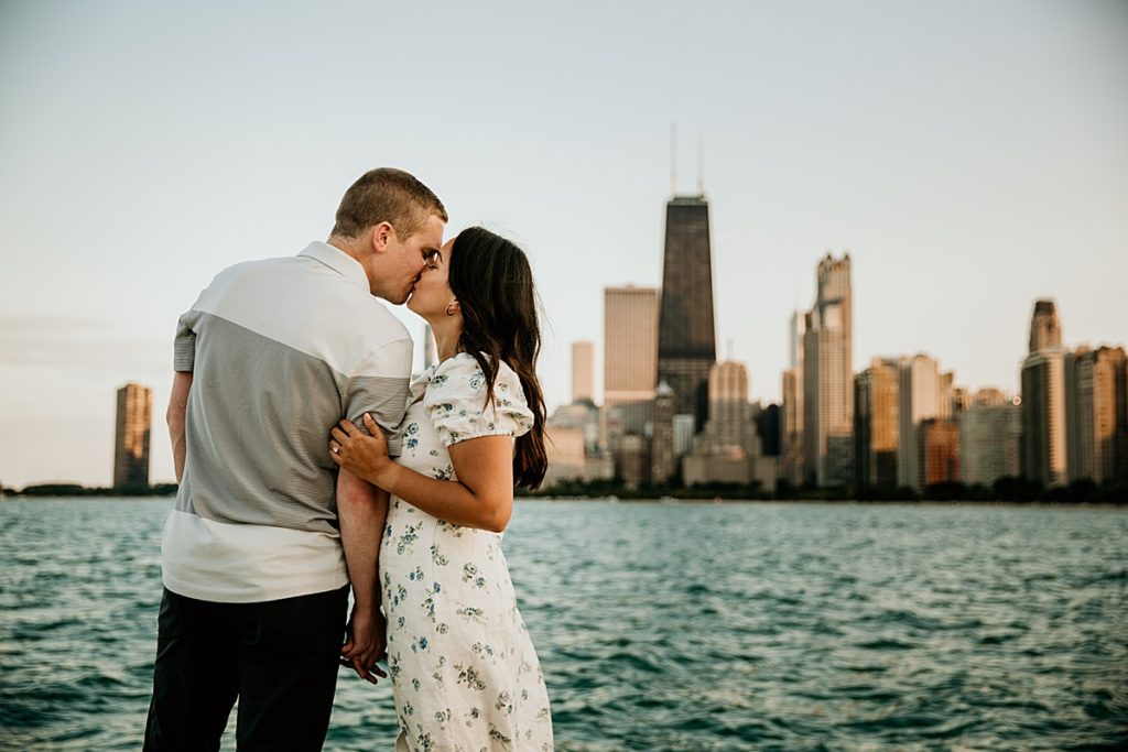Man and woman kissing by Lake Michigan with the chicago skyline behind them.
