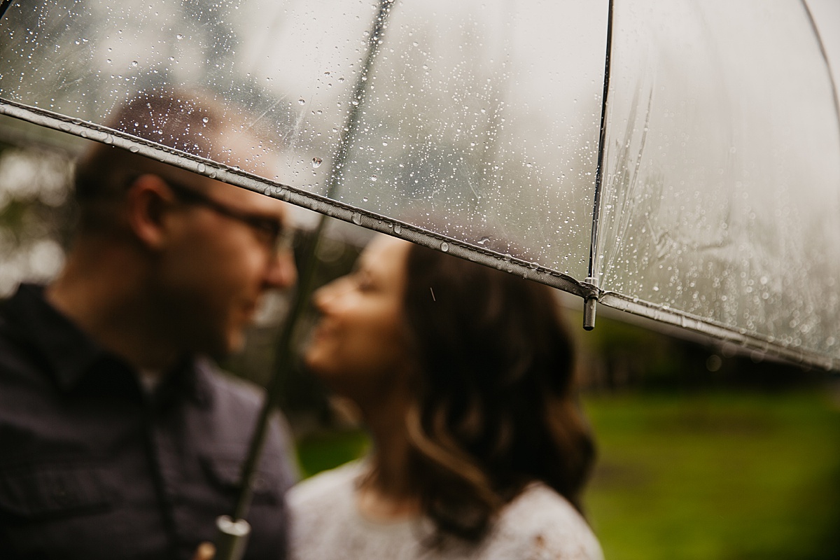 Couple snuggling under a clear umbrella on a rainy day.