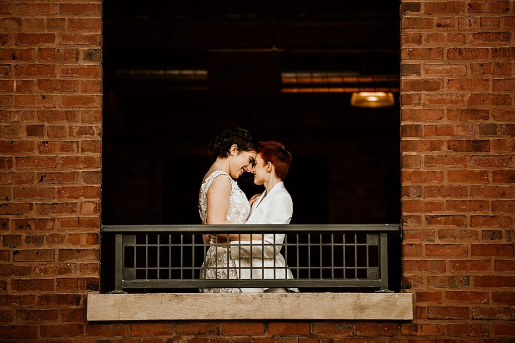Lesbian brides holding each other in a window balcony.