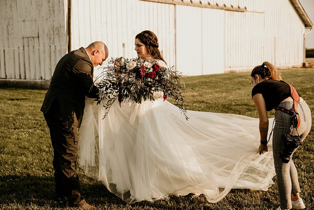 Photographer and groom helping the bride fluff her dress for photos. 