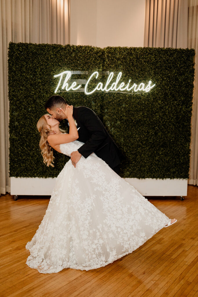 bride and groom kiss with neon name sign at wedding reception