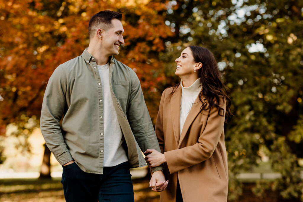 engaged couple walking in fall leaves at a park