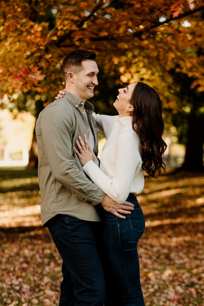 engaged couple laughing in fall leaves at a park